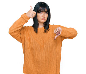 Canvas Print - Young hispanic woman wearing casual clothes doing thumbs up and down, disagreement and agreement expression. crazy conflict