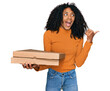 © Krakenimages.com - Young african american girl holding delivery pizza box pointing thumb up to the side smiling happy with open mouth