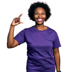 Poster - African american woman with afro hair wearing casual purple t shirt smiling and confident gesturing with hand doing small size sign with fingers looking and the camera. measure concept.