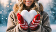 blonde woman holding a heart made of snow on a winter day - knitted mittens - boho background