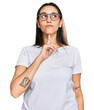 Young hispanic woman wearing casual white t shirt thinking concentrated about doubt with finger on chin and looking up wondering