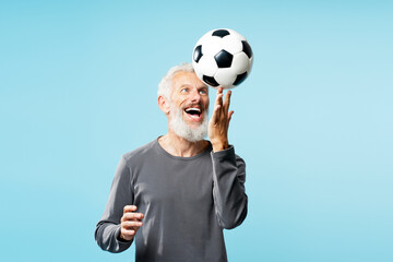 Excited bearded mature man holding soccer ball, having fun isolated on blue background. Sport, active lifestyle concept