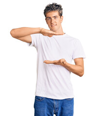 Wall Mural - Young handsome man wearing casual white tshirt gesturing with hands showing big and large size sign, measure symbol. smiling looking at the camera. measuring concept.