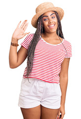 Sticker - Young african american woman with braids wearing summer hat waiving saying hello happy and smiling, friendly welcome gesture