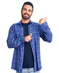 Sticker - Young hispanic man wearing casual clothes pointing to the back behind with hand and thumbs up, smiling confident