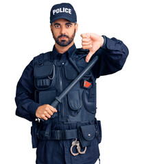 Wall Mural - Young hispanic man wearing police uniform holding baton with angry face, negative sign showing dislike with thumbs down, rejection concept