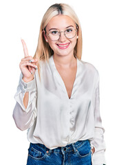 Wall Mural - Beautiful blonde woman wearing elegant shirt and glasses pointing finger up with successful idea. exited and happy. number one.