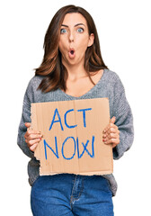 Sticker - Young brunette woman holding act now banner scared and amazed with open mouth for surprise, disbelief face