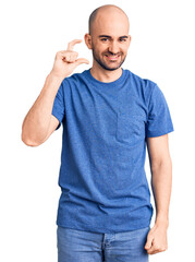 Canvas Print - Young handsome man wearing casual t shirt smiling and confident gesturing with hand doing small size sign with fingers looking and the camera. measure concept.