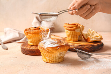 Wall Mural - Woman adding sugar powder onto tasty cruffins on beige background