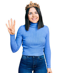 Poster - Young brunette woman with blue eyes wearing princess crown showing and pointing up with fingers number four while smiling confident and happy.