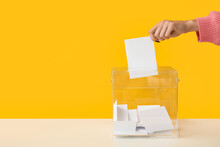 Hand Putting Voting Paper In Ballot Box On Yellow Background
