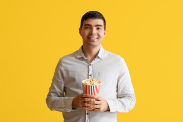 Wall Mural - Happy young man with popcorn on yellow background