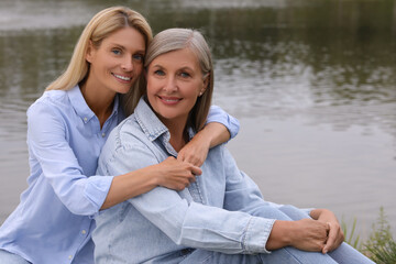 Wall Mural - Happy mature mother and her daughter hugging near pond