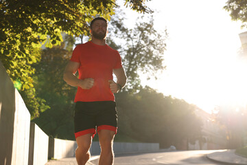 Canvas Print - Happy man running outdoors on sunny day, low angle view. Space for text