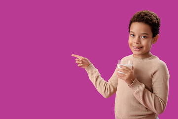 Little African-American boy with glass cup of milk pointing at something on purple background