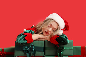 Poster - Sleepy young woman dressed as elf with Christmas gifts on red background