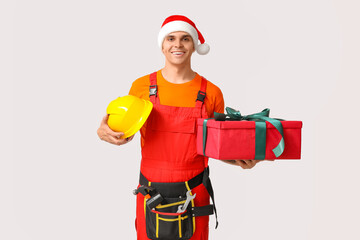 Poster - Handsome male builder in Santa hat with professional tools, gift box and hardhat on white background