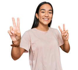 Wall Mural - Young asian woman wearing casual clothes smiling looking to the camera showing fingers doing victory sign. number two.