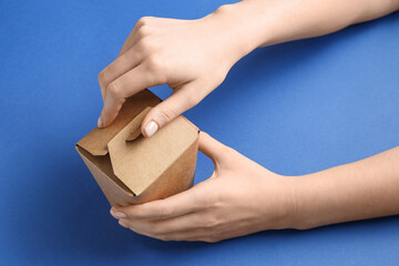 Wall Mural - Female hands with takeaway paper box on blue background