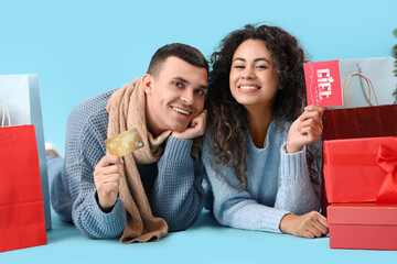 Sticker - Happy young couple with credit card, present boxes and shopping bags lying on blue background