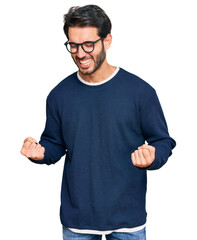 Sticker - Young hispanic man wearing casual clothes and glasses very happy and excited doing winner gesture with arms raised, smiling and screaming for success. celebration concept.