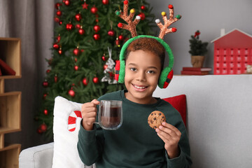 Poster - Little African-American boy in reindeer horns eating cookie with hot chocolate at home on Christmas eve