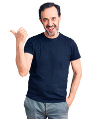 Wall Mural - Middle age handsome man wearing casual t-shirt smiling with happy face looking and pointing to the side with thumb up.