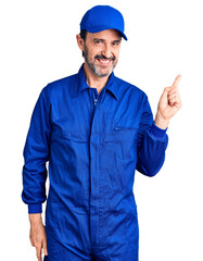 Wall Mural - Middle age handsome man wearing mechanic uniform with a big smile on face, pointing with hand finger to the side looking at the camera.