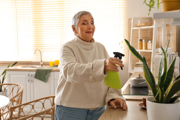 Poster - Senior woman watering plant in kitchen