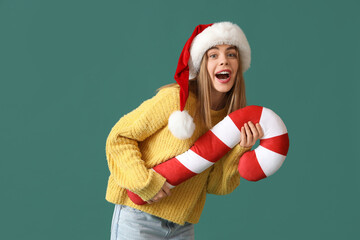 Sticker - Happy young woman in Santa hat with candy cane pillow on green background