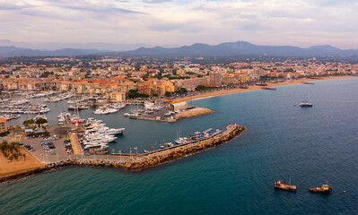 Wall Mural - Picturesque aerial view of coastal area of Frejus overlooking marina with moored pleasure yachts and residential districts along waterfront in warm autumn day, France