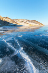 Wall Mural - Scenic winter landscape of frozen Baikal Lake on cold January day. View of snowy coastal hills in light of setting sun and icy bay with blue ice surface with cracks. Winter ice travel and outdoors