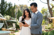 © bongkarn - Happy young Asian couple watching videos on a smartphone while walking in a garden together.