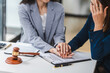 © NanSan - Two middle aged and young Asian lawyer in a formal suit consoles a client during a legal consultation, with a gavel and documents on the table.