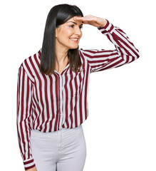 Wall Mural - Beautiful brunette woman wearing striped shirt very happy and smiling looking far away with hand over head. searching concept.