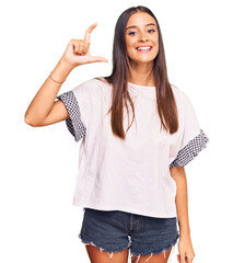 Wall Mural - Young hispanic woman wearing casual clothes smiling and confident gesturing with hand doing small size sign with fingers looking and the camera. measure concept.