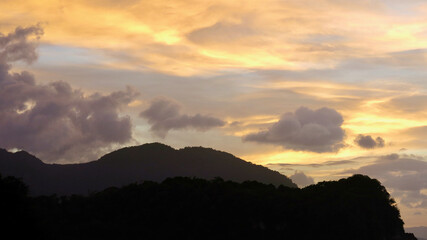 Wall Mural - Sunset over the mountains. Sunset over the sea and tropical island. The sun behind the clouds sets below the horizon. The sun's rays color the sky and clouds during sunset.