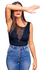 Wall Mural - Young hispanic woman wearing casual clothes covering eyes with arm, looking serious and sad. sightless, hiding and rejection concept