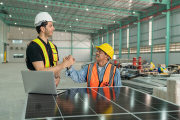 Two engineers in safety vests shaking hands after completing solar panel installation inside an industrial warehouse, symbolizing teamwork and project success.