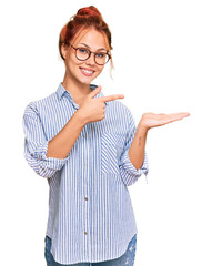 Poster - Young redhead woman wearing casual clothes and glasses amazed and smiling to the camera while presenting with hand and pointing with finger.