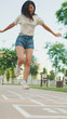 © Andrii Nekrasov - Joyful beautiful brunette girl dressed in casual clothes playing hopscotch game outdoors, having fun