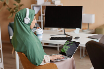 Side view portrait of Muslim young woman as female programmer writing code and wearing headscarf in office, copy space