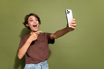 Poster - Photo portrait of lovely young lady hold device selfie point finger smile dressed stylish brown garment isolated on khaki color background