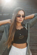 © alones - Beautiful glamorous young stylish woman model with sunglasses in fashion clothes with a green shirt with a black top stands near a black brick wall. Pretty chic street girl at sunset