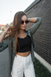 © alones - Beautiful young fashion girl with sunglasses in fashionable clothes near a black brick wall in the city