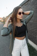 © alones - Elegant beautiful street model girl with vintage sunglasses in fashion clothes stands and straightens her hair near a black brick wall. Pretty chic lady
