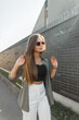 © alones - Beautiful young fashion woman model with sunglasses in fashionable clothes with shirt walks on a sunny day in the city near a black brick wall