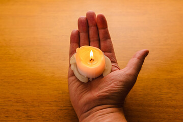 Wall Mural - Burning candle on the palm.Man holding lighted wax candle on a wooden background.Male holding a candle in the dark.