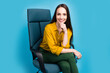 Photo of clever positive woman dressed yellow shirt sitting armchair arm chin isolated blue color background